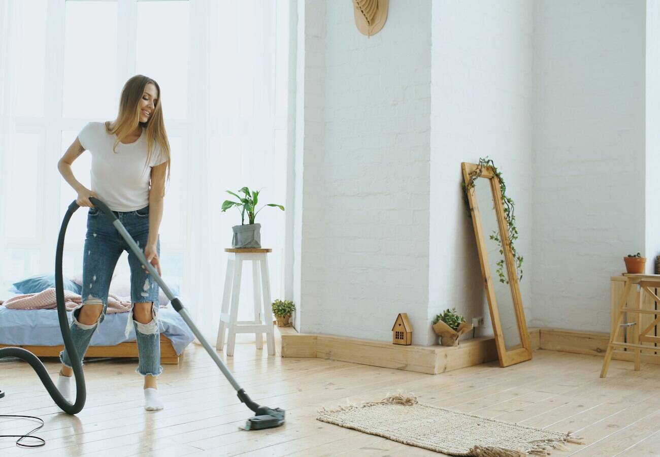 A cleaner vacuuming the floor of a bright, sparsely furnished room.