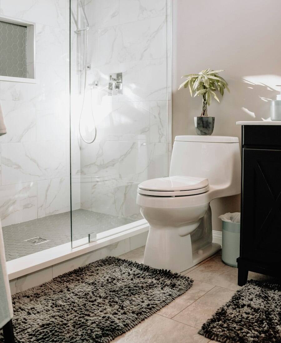 A clean bathroom with a marble-tiled glass shower and a small plant.